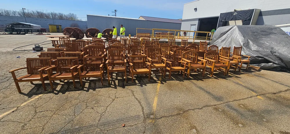 Large group of of teak chairs being refinished outside of an industrial warehouse.